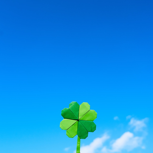 Green paper origami folded shamrock on blue sky background. Sunny weather outdoors. Sapce for text, lettering, copy. - Zdjęcie, obraz