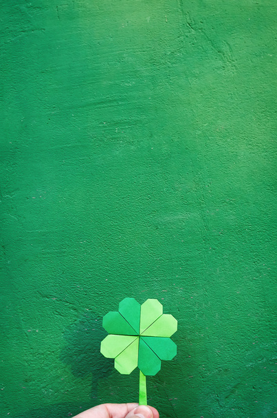 Hand holding paper origami green shamrock on wall background. Space for copy, lettering, text. St. Patrick's day postcard tempalte. - Foto, afbeelding
