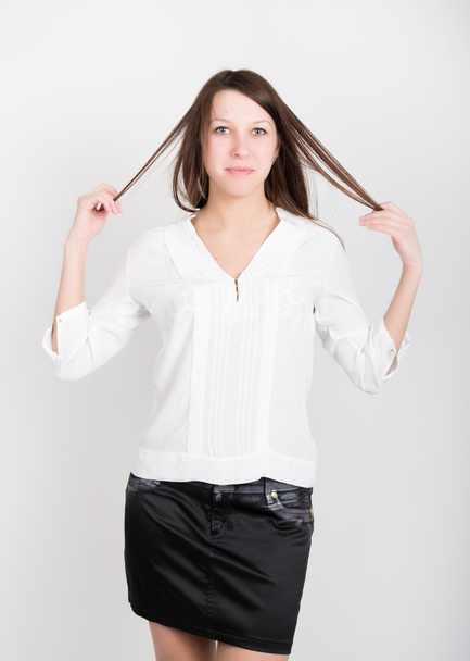 Menina fina bonita em uma saia preta curta e blusa branca, segurando seu cabelo
 - Foto, Imagem
