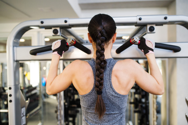 Woman in gym flexing back muscles on cable machine - Foto, Bild