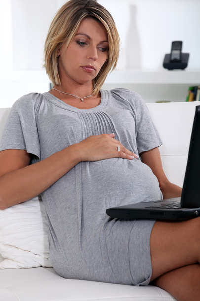 Pregnant woman looking at a laptop - Foto, afbeelding