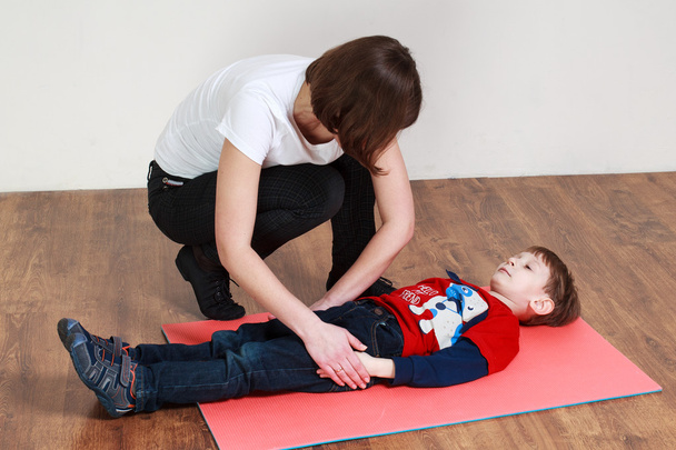  Little boy is lying on the mat at a gym, trainer is helping him - Valokuva, kuva