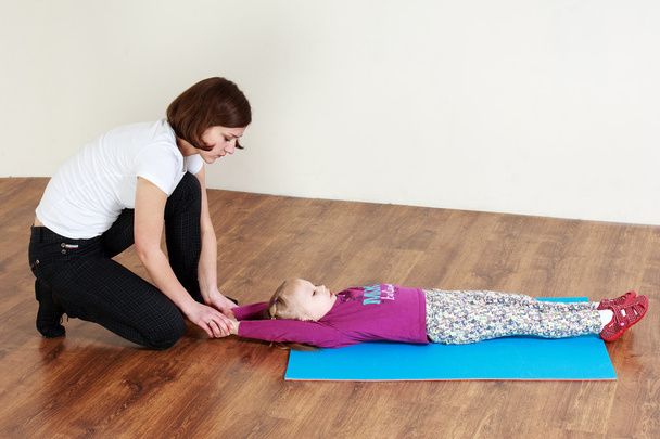 Trainer sta facendo stretching con una bambina sdraiata su un tappeto
  - Foto, immagini