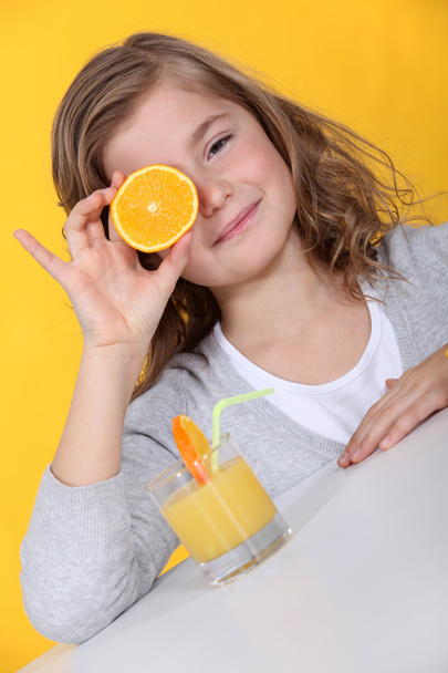 Girl covering her eye with orange slice - Фото, изображение