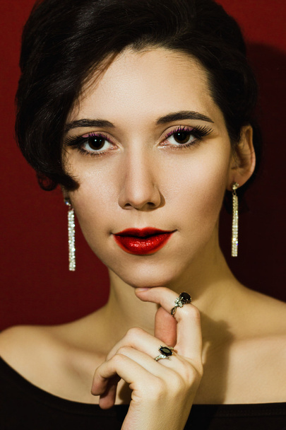 Porträt eines schönen jungen Mädchens im Schmuck auf rotem Hintergrund. elegante Frau mit Diamantohrringen und Ringen. - Foto, Bild