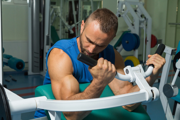 The athlete does bench biceps on the simulator in the gym. Hand muscle training on the simulator. Tense muscles of hands under load. Photos for sporting magazines, posters and websites. - Photo, Image